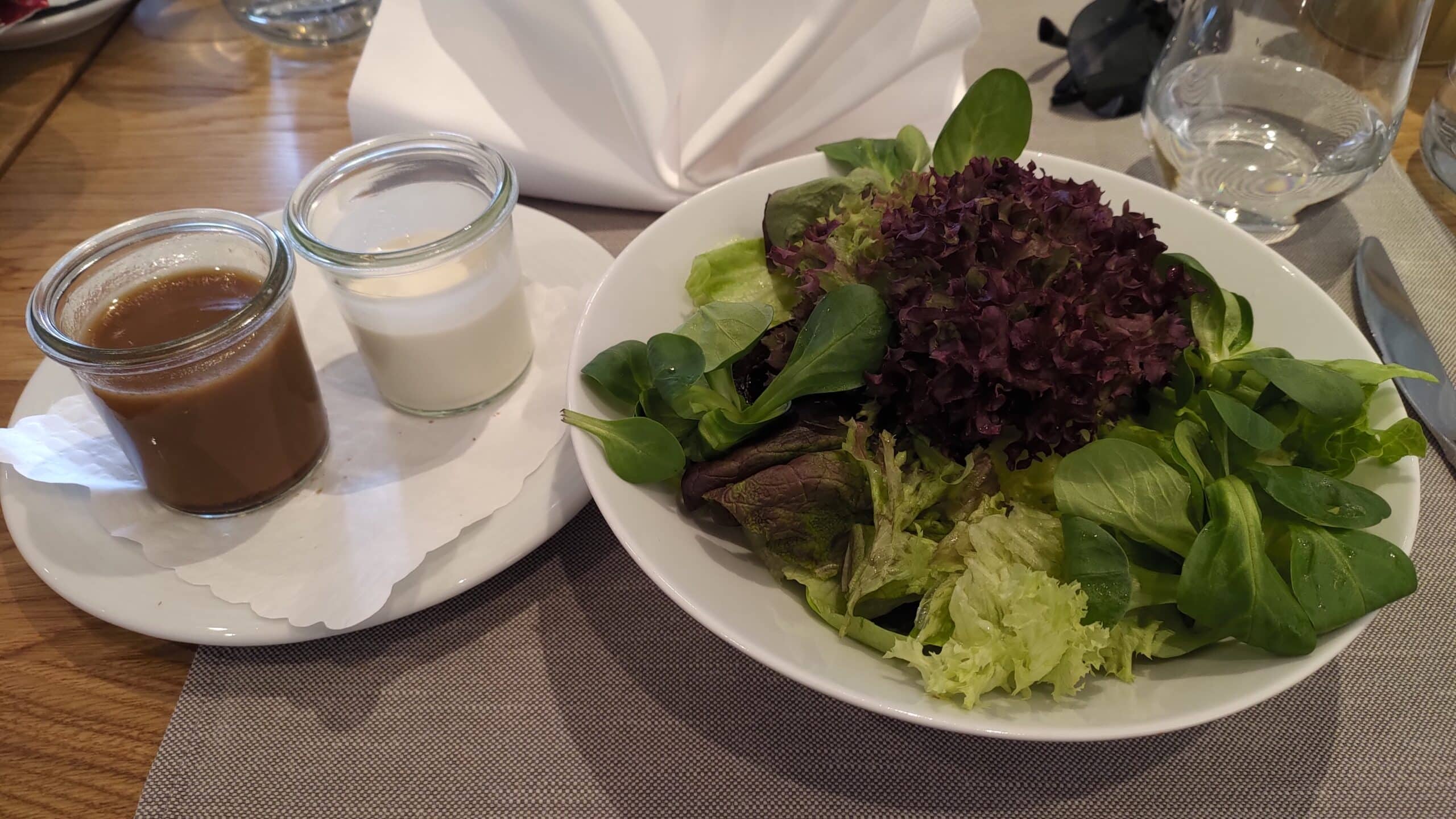 Teller mit grünem Salat neben zwei Schüsselchen mit Salatsauce